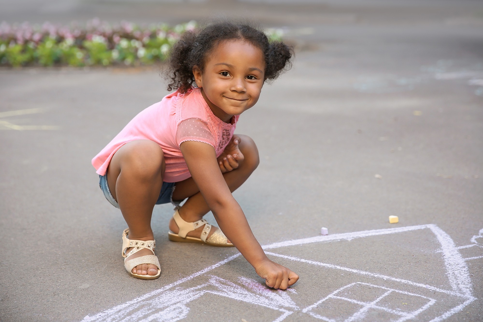 Little African-American child drawing house with chalk on asphal